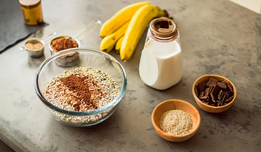 Rustic kitchen setup with Chocolate Banana Protein Baked Oatmeal ingredients: rolled oats, chocolate protein powder, mashed bananas, plant-based milk, dark chocolate chips, and vanilla extract, arranged with warm natural light.