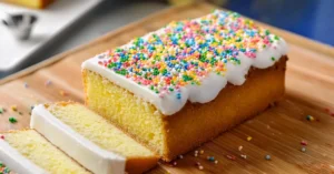 Classic school cake recipe: a vanilla sponge topped with white icing and colorful sprinkles, sliced into squares for a nostalgic treat.