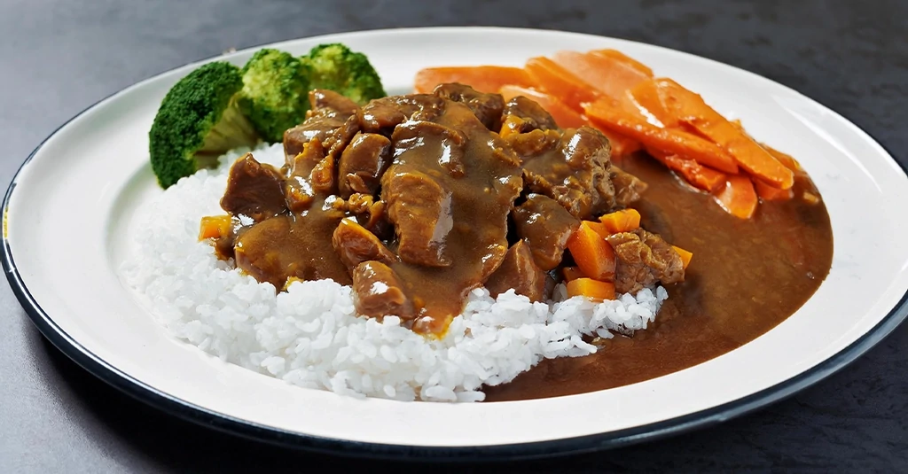 Plate of crockpot beef tips and gravy served over white rice with a side of steamed broccoli and carrots, garnished with fresh green onions for a hearty, comforting meal.